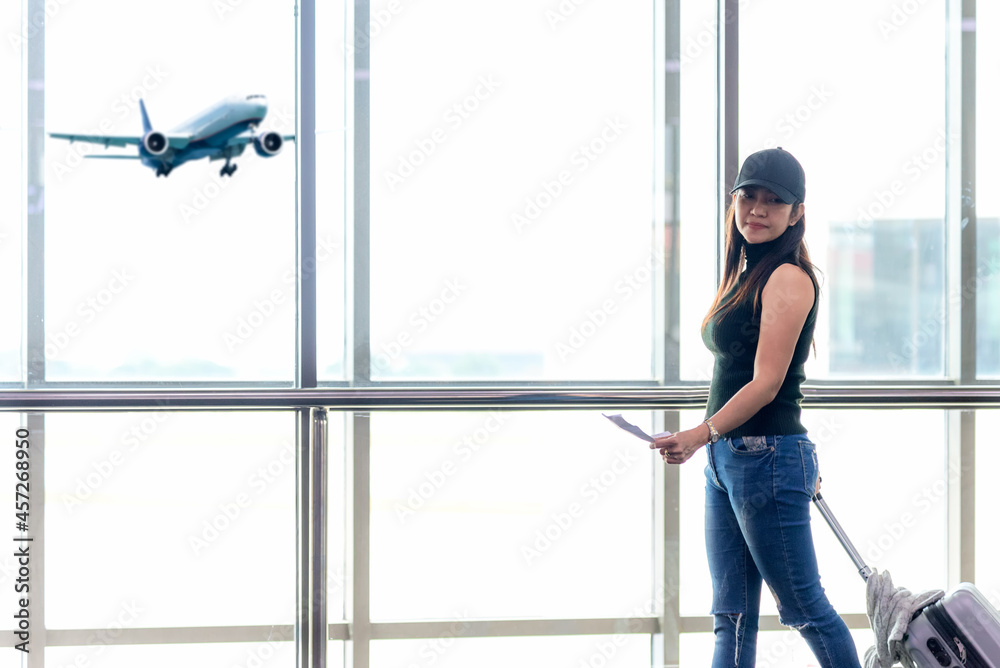 Traveler woman plan and backpack see airplane flight at the airport glass window, girl tourist happy hold bag and waiting luggage in hall airplane departure. Business people trip and Travel Concept
