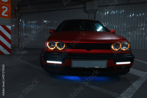 Stylish red old car with new tuning and LED headlights in the parking lot at night © alones
