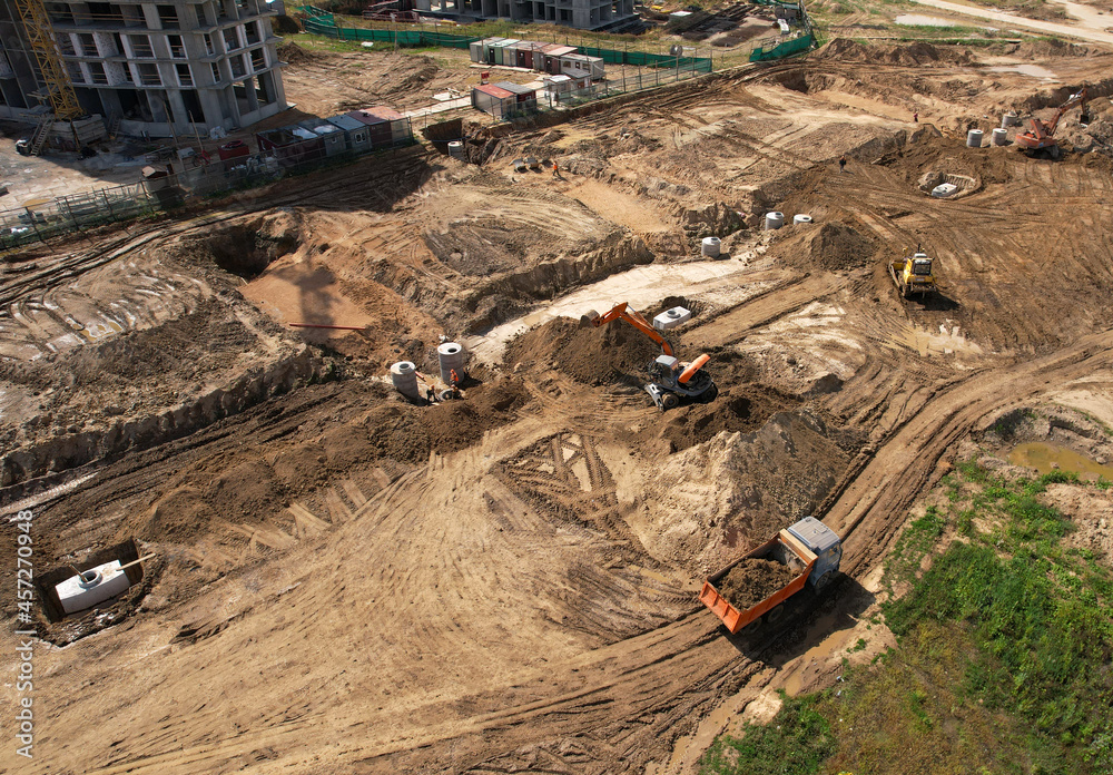 Obraz premium Laying a concrete well ring and sewer pipe at construction site. Earthworks during the install of storm sewers. Sanitary sewer. Dig ground for sewerge construction. Sewage drainage and concrete pipes.