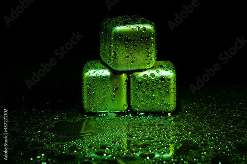 Green stainless steel cubes simulating ice for cooling drinks on a black surface with a reflection.