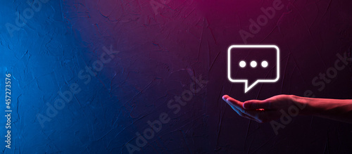 Hand on neon background holding a message icon, bubble talk notification sign in his hands. Chat icon, sms icon, comments icon, speech bubbles