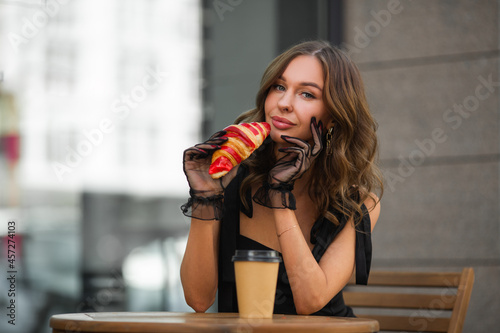 beautiful female in a dress with a croissant and coffee in a summer cafe 