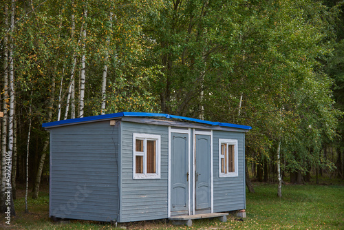 A small summer house stands in a clearing against the background of birch trees. © FO_DE
