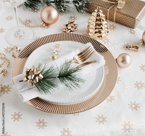 Christmas or New Year table setting with white golden tableware and cutlery , decorations top view on white linen tablecloth , copy space. flat lay.