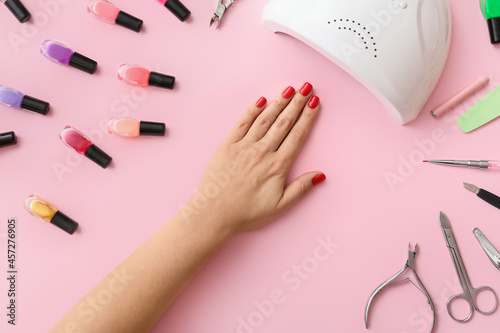 Female hand with tools for manicure and nail polishes on color background