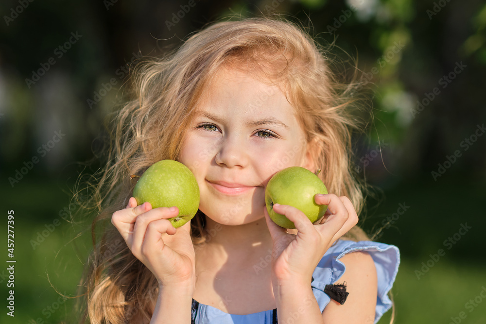 Little girl smiles at the camera. pretty girl posing for a photo and holding two green fresh apples in her hands Little girl smiles at the camera. pretty girl posing for a photo and holding two green fresh apples in her hands