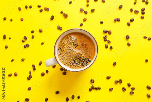 Cup of coffee and scattered beans on color background