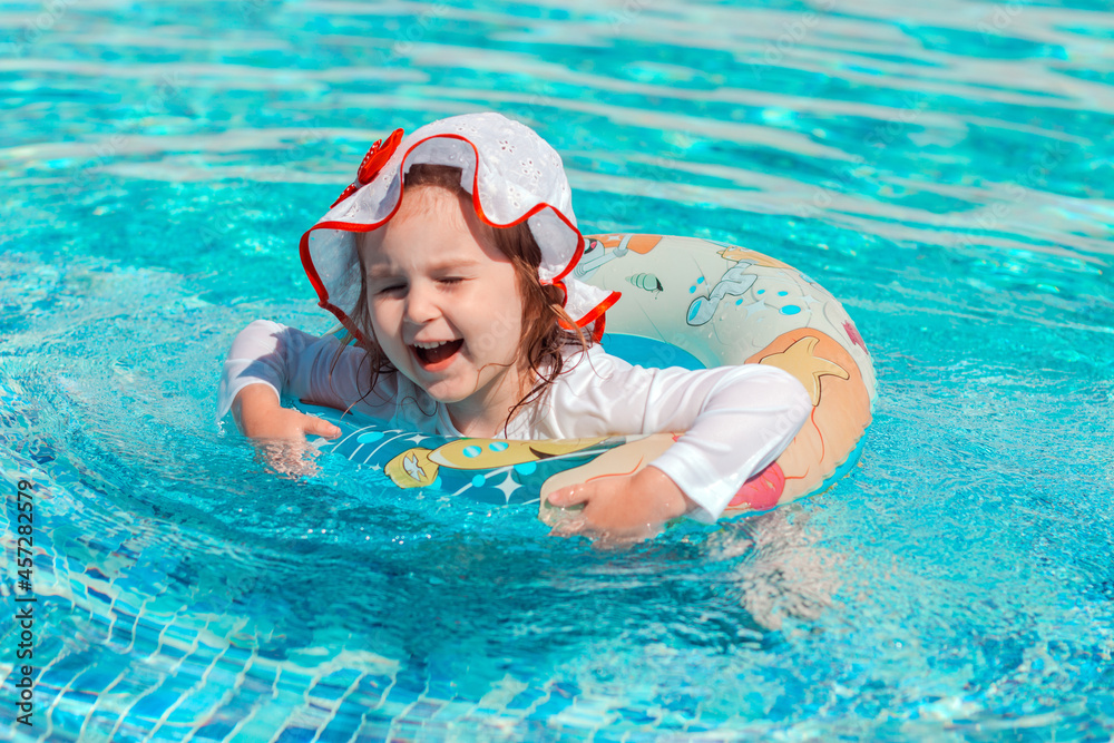 Little girl swimming in pool in white swimwear with sun protection. Healthy and safe summer outdoor activities.