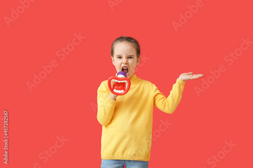 Angry little girl shouting into megaphone on color background photo