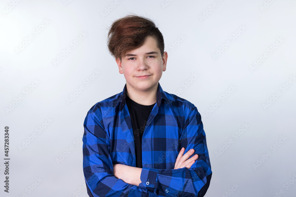 A teenage boy stands on a light background in a blue shirt and looks at the camera. he is Caucasian. He's happy. Horizontally. There is a place for the text. Copy space. A teenage boy stands on a light background in a blue shirt and looks at the camera. he is Caucasian. He's happy. Horizontally. There is a place for the text. Copy space.