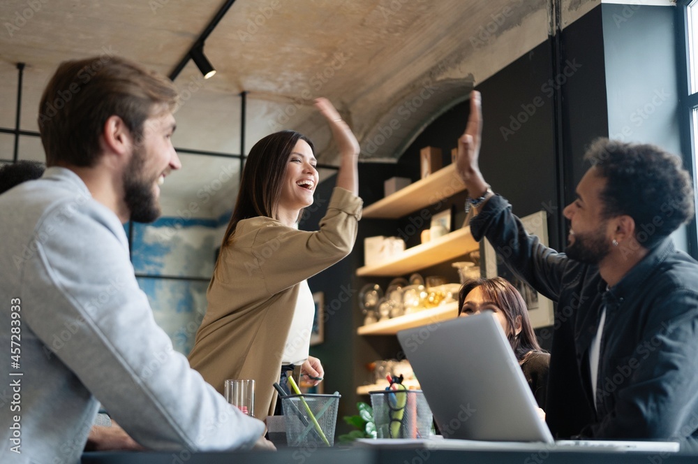 Two cheerful young business people giving high-five while their colleagues looking at them and smiling. - obrazy, fototapety, plakaty 