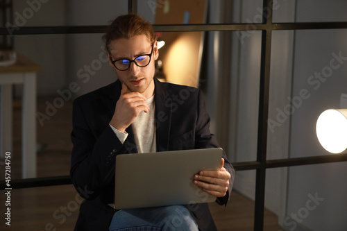 Thoughtful young man using laptop in office at night