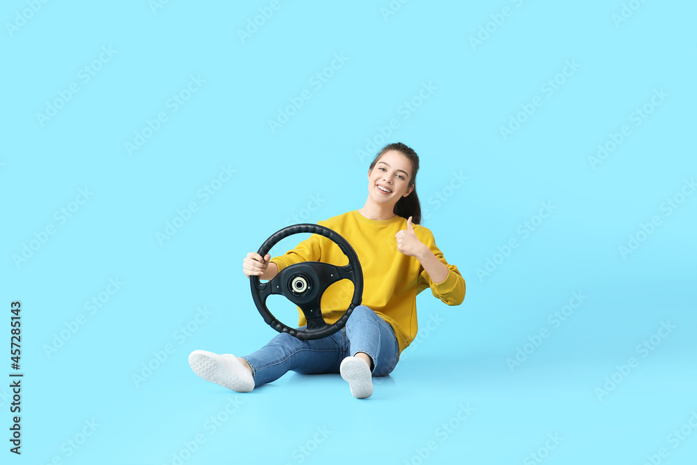 Young woman with steering wheel showing thumb-up on color background Young woman with steering wheel showing thumb-up on color background