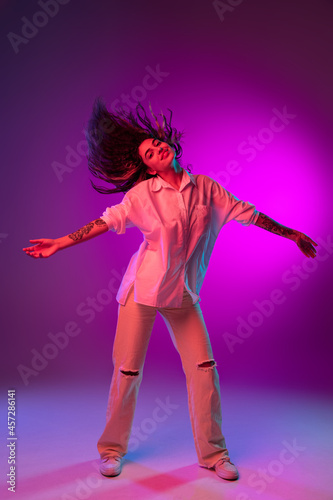 Portrait of Latino beautiful happy girl dancing isolated on purple, lilac color studio background in neon light. Concept of human emotions, facial expression
