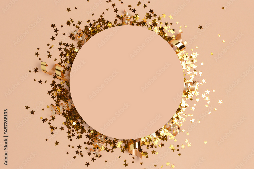 Round frame made of gold colored confetti on a beige background.