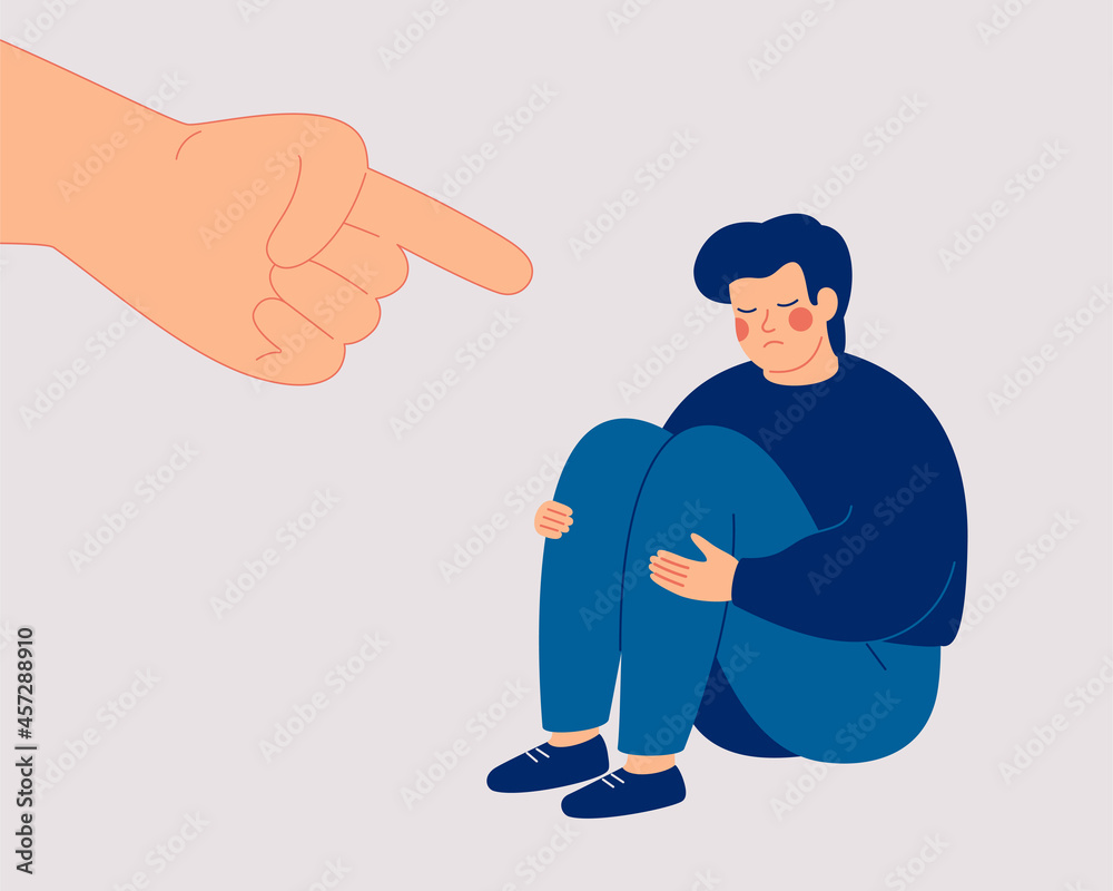 Sad boy suffers from psychological abuse from his peers. Depressed man sits on the floor and a big hand with an index finger is pointing at his. Public censure and victim-blaming. Bullying concept.