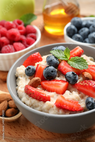 Tasty oatmeal porridge with berries and almond nuts in bowl served on wooden board