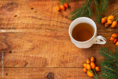 winter, warm atmosphere. A cup of hot black tea with a red scarf, rose berries and spruce on a wooden background