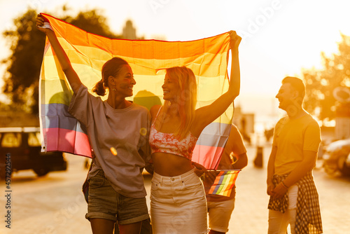 Young lesbian couple walking with rainbow flags during pride parade