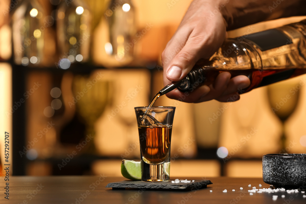 Bartender pouring tasty tequila into glass at table in bar