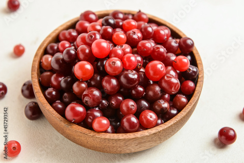 Bowl with healthy cranberries on light background