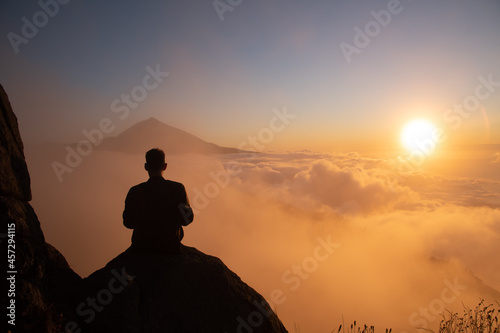Boy looking at a sunset with the Teide volcano above the clouds and the sun hiding between them.