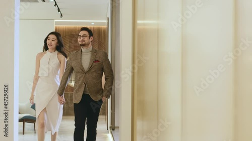 Asian happy upscale couple walking in hallway hand in hand smiling