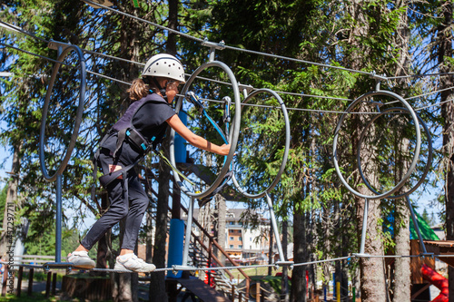 Little girl in safety equipment at adventure amusement park. Child having fun outdoor