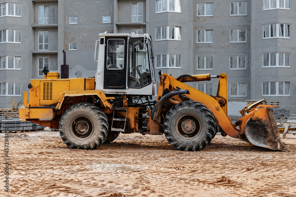 Heavy wheel loader with a bucket at a construction site. Equipment for earthworks, transportation and loading of bulk materials - earth, sand, crushed stone.