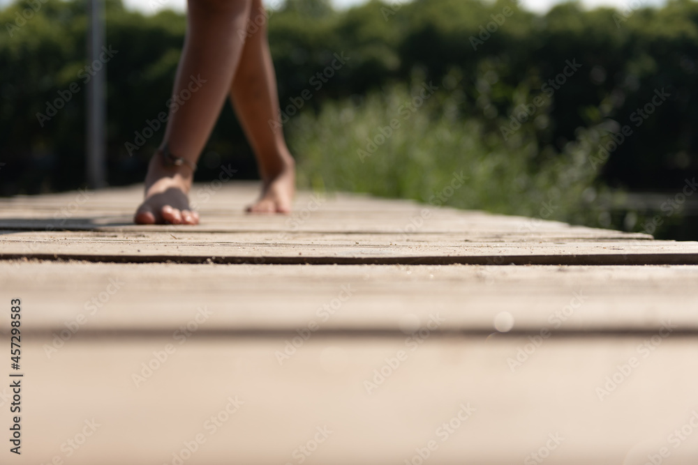 woman legs walking on a floating wooden dock in the river, followed by a boy.