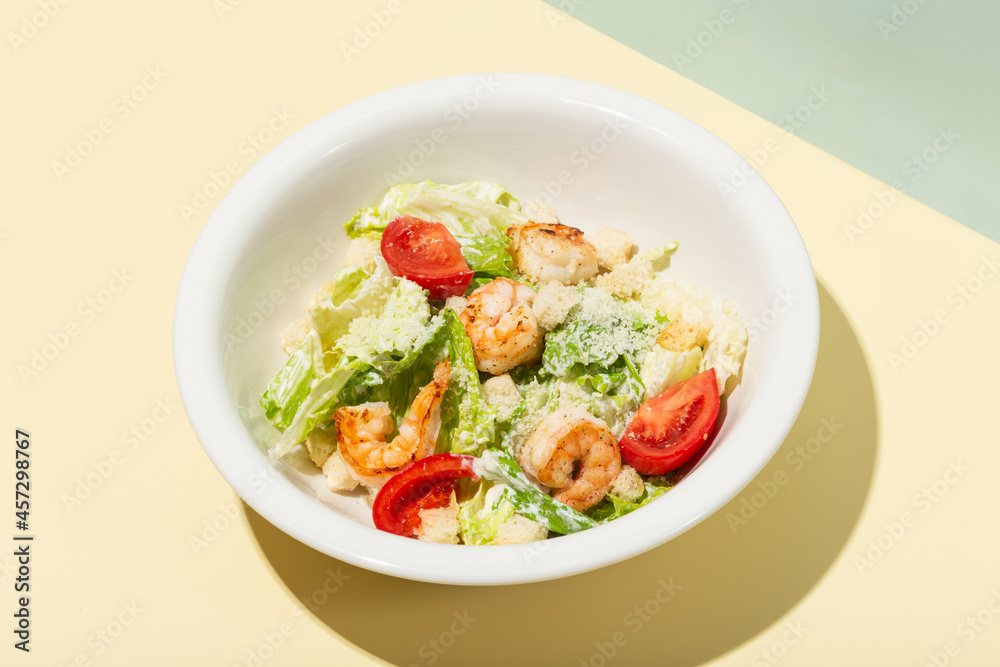 Caesar salad with shrimp in white plate on yellow hard shadow modern Caesar salad with shrimp in white plate on yellow hard shadow modern