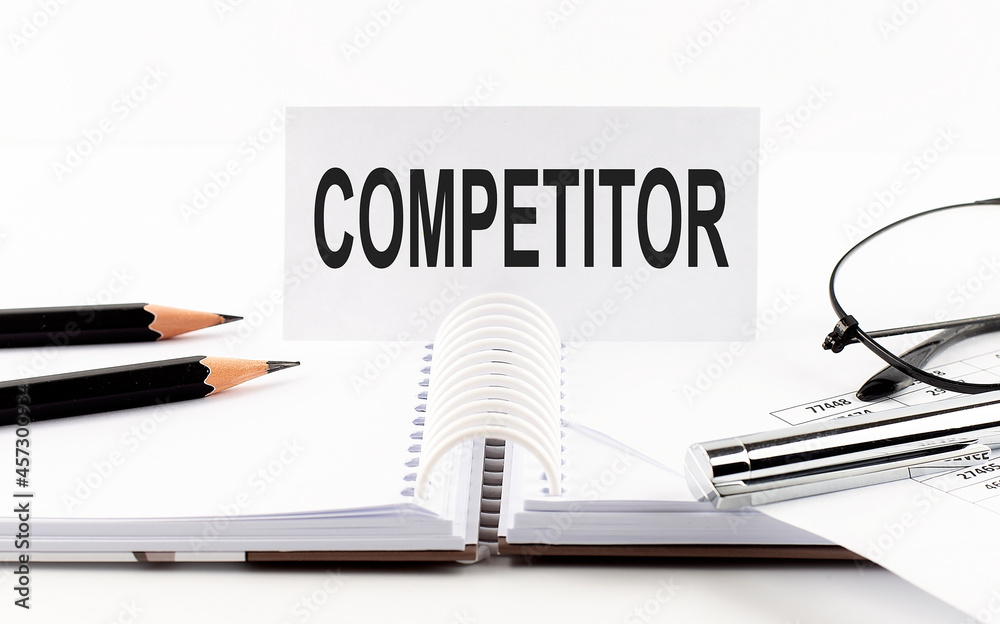Text COMPETITOR on paper card,pen, pencils, glasses,financial documentation on table - business concept Text COMPETITOR on paper card,pen, pencils, glasses,financial documentation on table - business concept