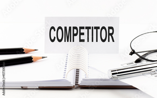 Text COMPETITOR on paper card,pen, pencils, glasses,financial documentation on table - business concept