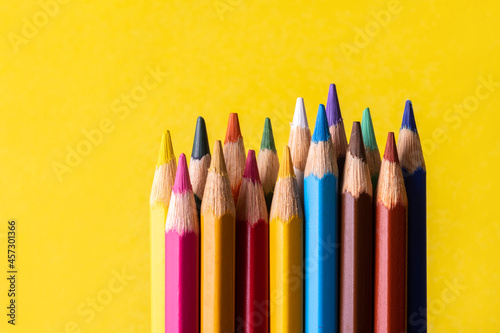 Set of wooden colored pencils on a yellow sheet of paper background