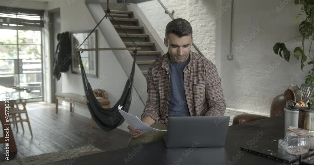 Mid adult hispanic male using laptop in kitchen Mid adult hispanic male using laptop in kitchen