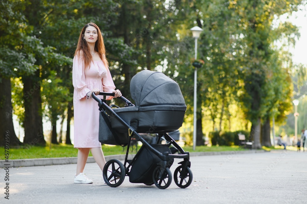 Happy young mother with baby in buggy walking in autumn park Happy young mother with baby in buggy walking in autumn park