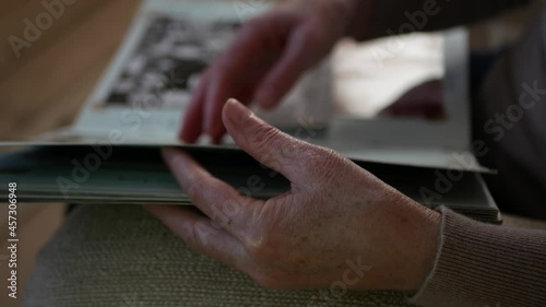 Adult woman looks old photo album at home. Close up view of aged woman's hand with old photo album. Elderly person is leafing through photo album.