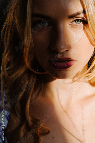 Portrait of a beautiful young attractive blonde girl. Play of light and shadow. Half of the face is in the shade. Piercing gaze
