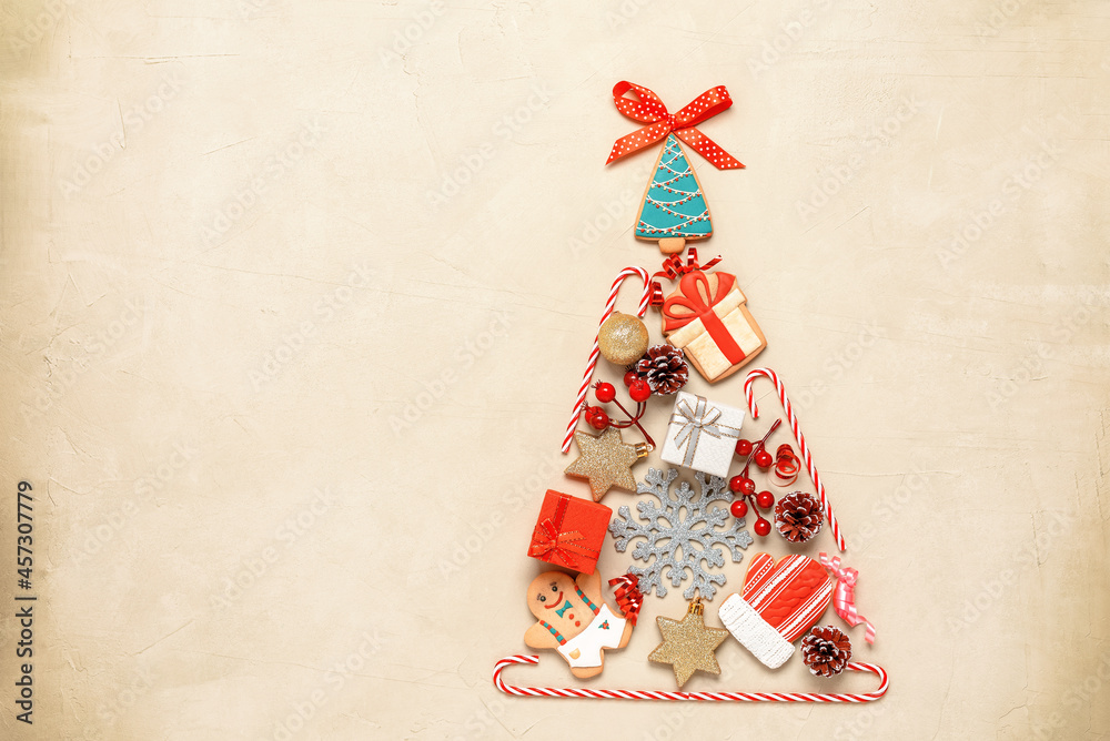 Abstract Christmas tree flat lay on beige concrete background. Christmas tree made of gingerbread, candy cane, ball, star, pine cone and gift box. Top view.
