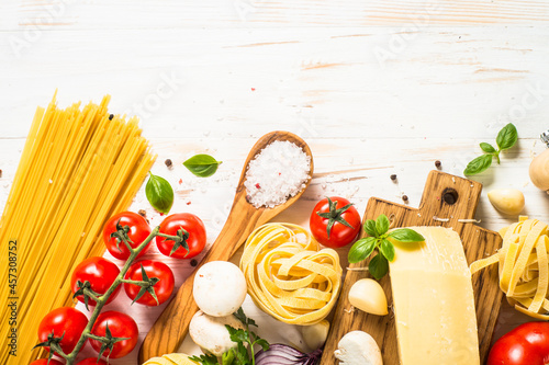 Italian food background on white wooden table. Pasta, fresh tomatoes, spices and basil. Top view with copy space.