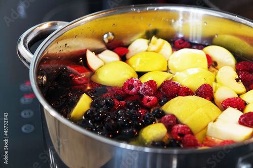 We are preparing a delicious compote from apples, cherries, raspberries, irgi. Fresh fruits and berries are boiled in a metal pan on the stove.