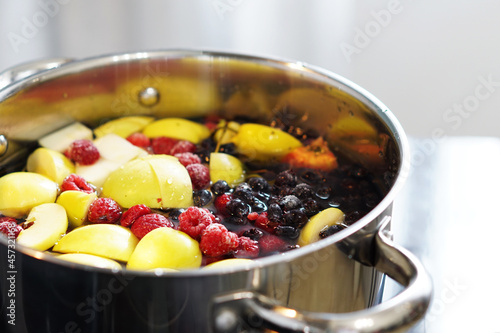 We are preparing a delicious compote from apples, cherries, raspberries, irgi. Fresh fruits and berries are boiled in a metal pan on the stove.