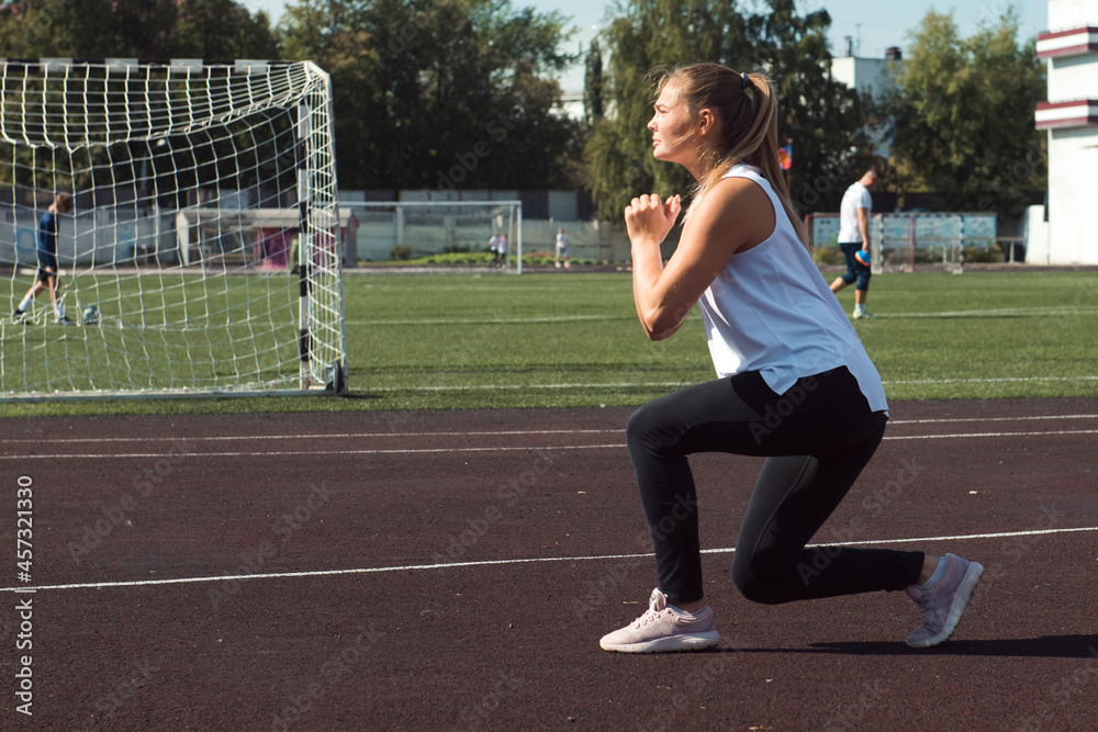 Young sporty woman doing lunges exercises at stadium