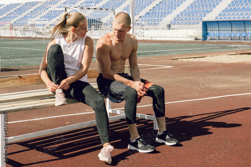 Young couple shirtless man and woman relaxing after workout at stadium, smiling and talking