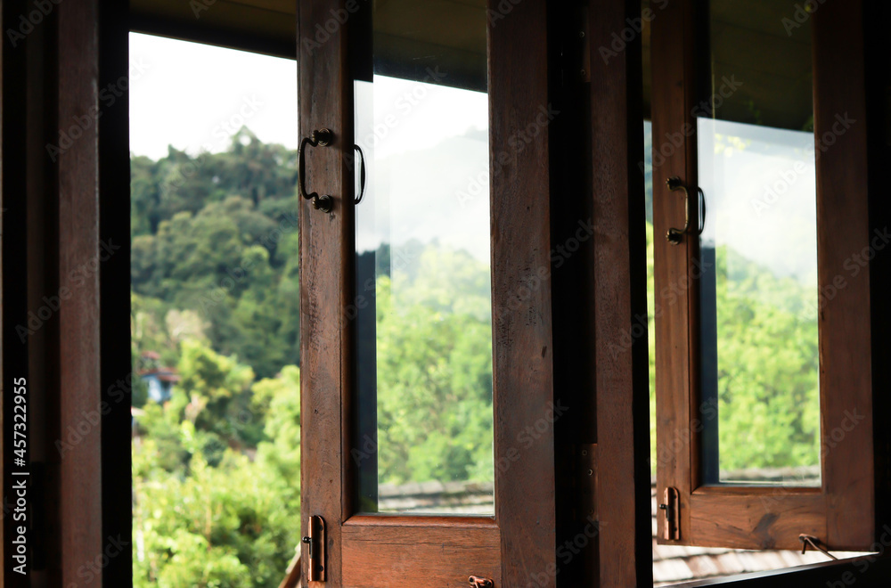 Fototapeta premium Dark brown wooden window open and outside is blurry scenery of green mountain.