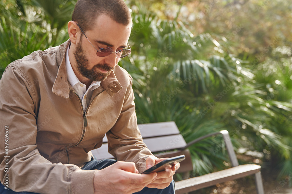 Fototapeta premium A straight faced man sitting on a bench texting