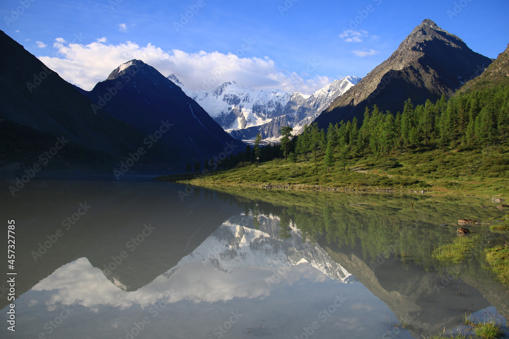 Alpine valley of the Ak-Kem river with a view of the snow-covered Belukha mountain, morning, in the foreground the reflection of the mountains in the river and the forest, in the background Belukha