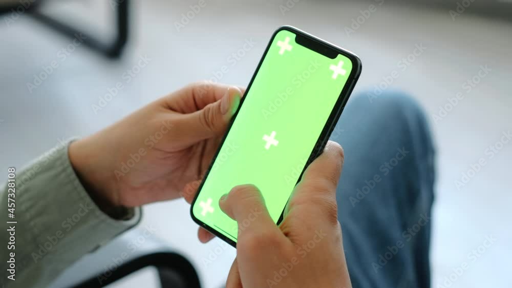 Man sitting in armchair at home and uses smartphone with green screen Mock-up. 4k