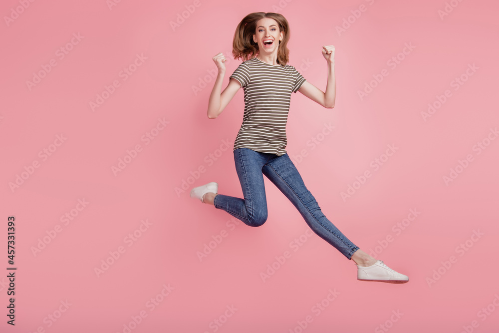Full body portrait of young woman happy positive smile rejoice victory fists hands jump up isolated over pink color background Full body portrait of young woman happy positive smile rejoice victory fists hands jump up isolated over pink color background