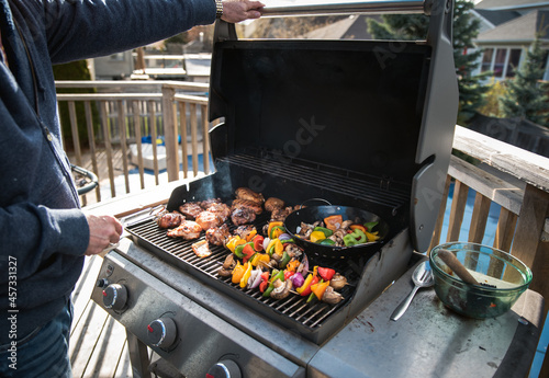 Foto Man grilling chicken and vegetables outdoors on a gas bbq grill.